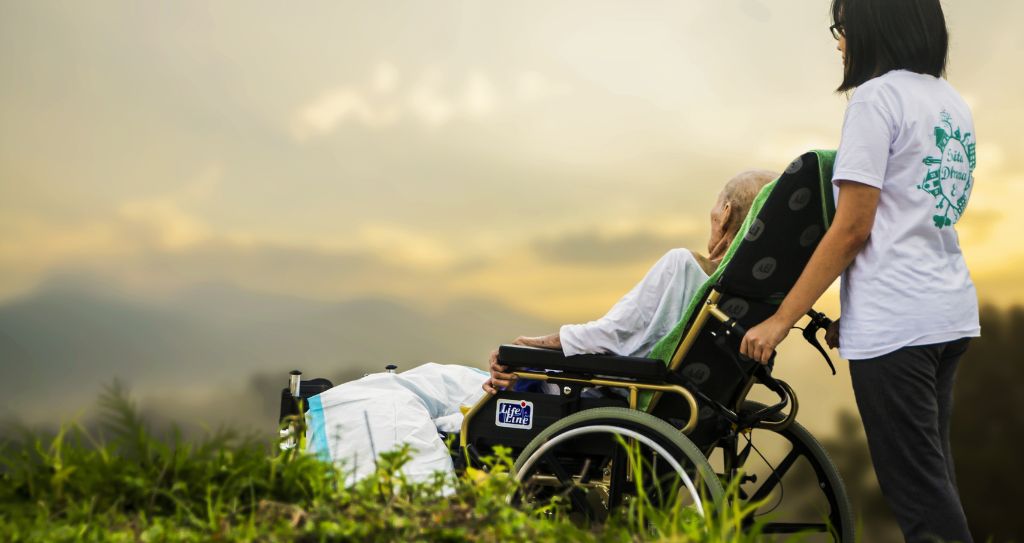 hospice caregiver assisting an old man sitting in a wheelchair